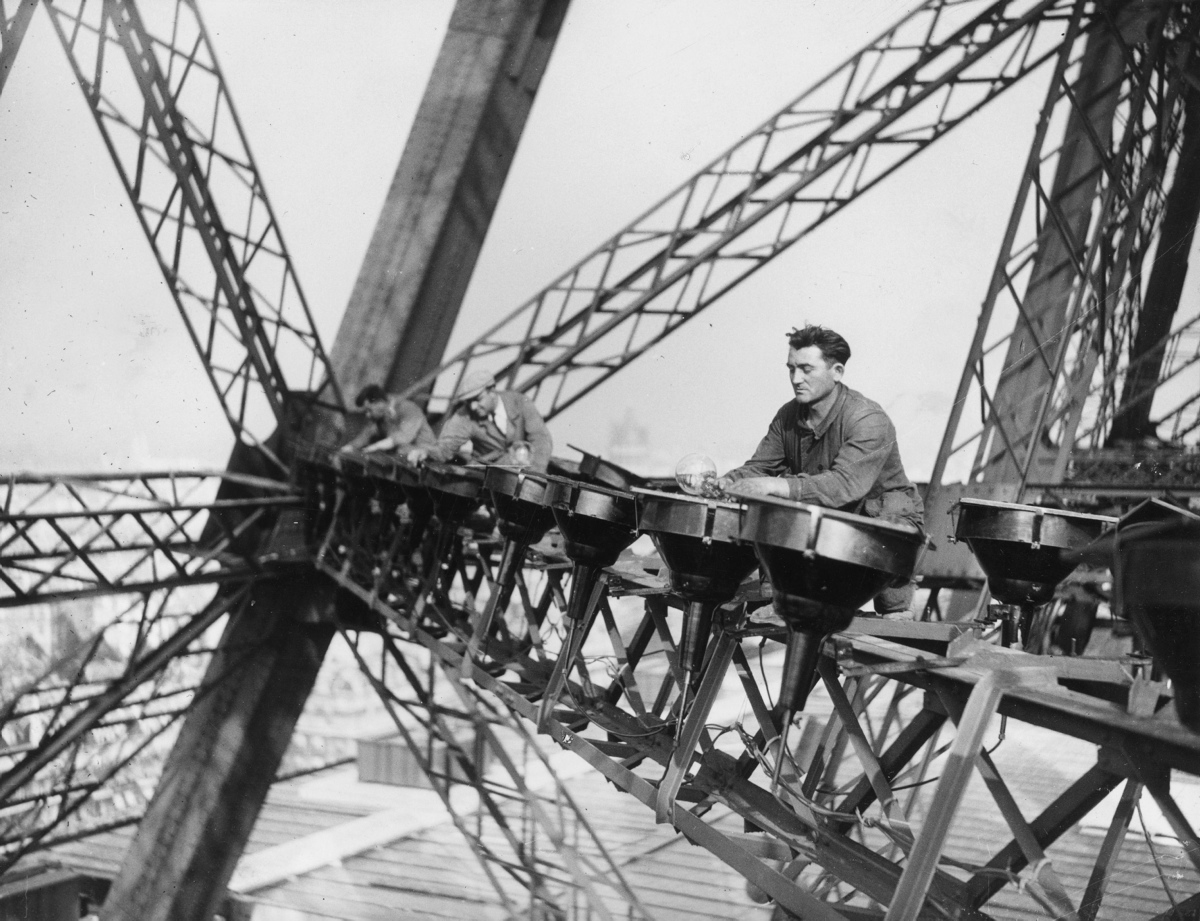Electrical workers balance high up on the Eiffel tower in paris to change the lights that illuminate the tower at night on Oct. 29, 1937.