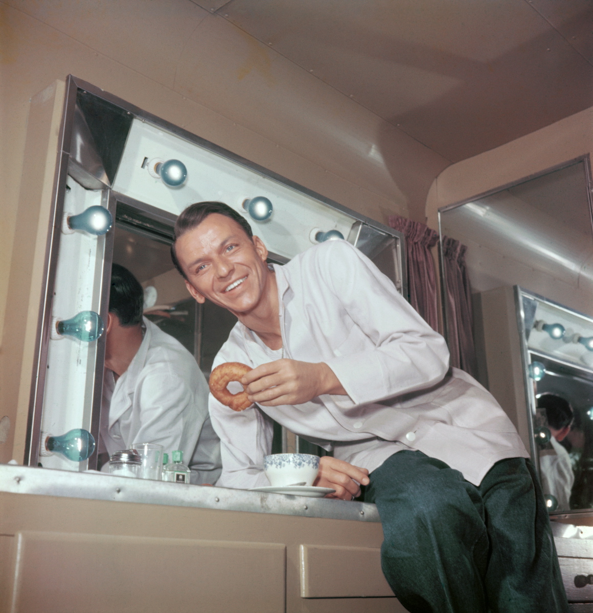 Frank Sinatra was all smiles in this photo of him enjoying coffee and donuts in his trailer during a break in filming, circa 1950.